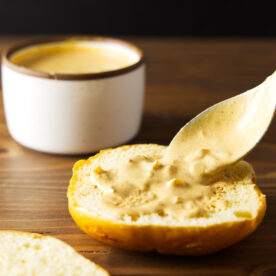 Burger sauce spreading on burger bun using a spoon on a wooden counter.