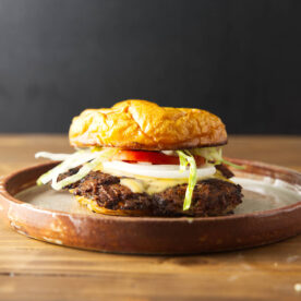 Smash burger with melty cheese, onion, tomato, and lettuce plated on a brown ceramic plate.