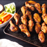 Square image of smoked chicken wings with carrots and celery sticks.