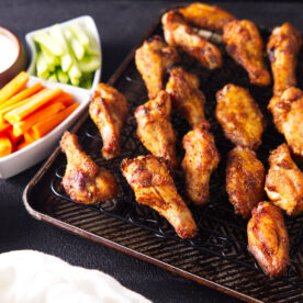 Square image of smoked chicken wings with carrots and celery sticks.