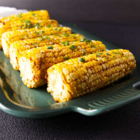 Smoked corn on the cob on a green ceramic platter.