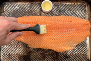 Brushing salmon fillet with olive oil on a sheet pan.