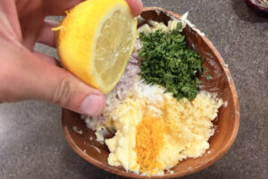 Squeezing lemon juice in to compound butter mixture in a wooden bowl.