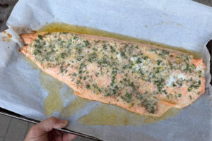 Removing salmon fillet from the grill on a sheet pan.