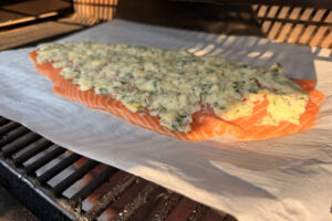 Fillet of salmon with compound butter spread on top and sitting on the grill grates.
