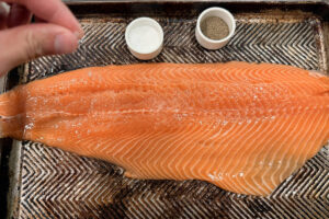 Seasoning a salmon fillet with salt and pepper.