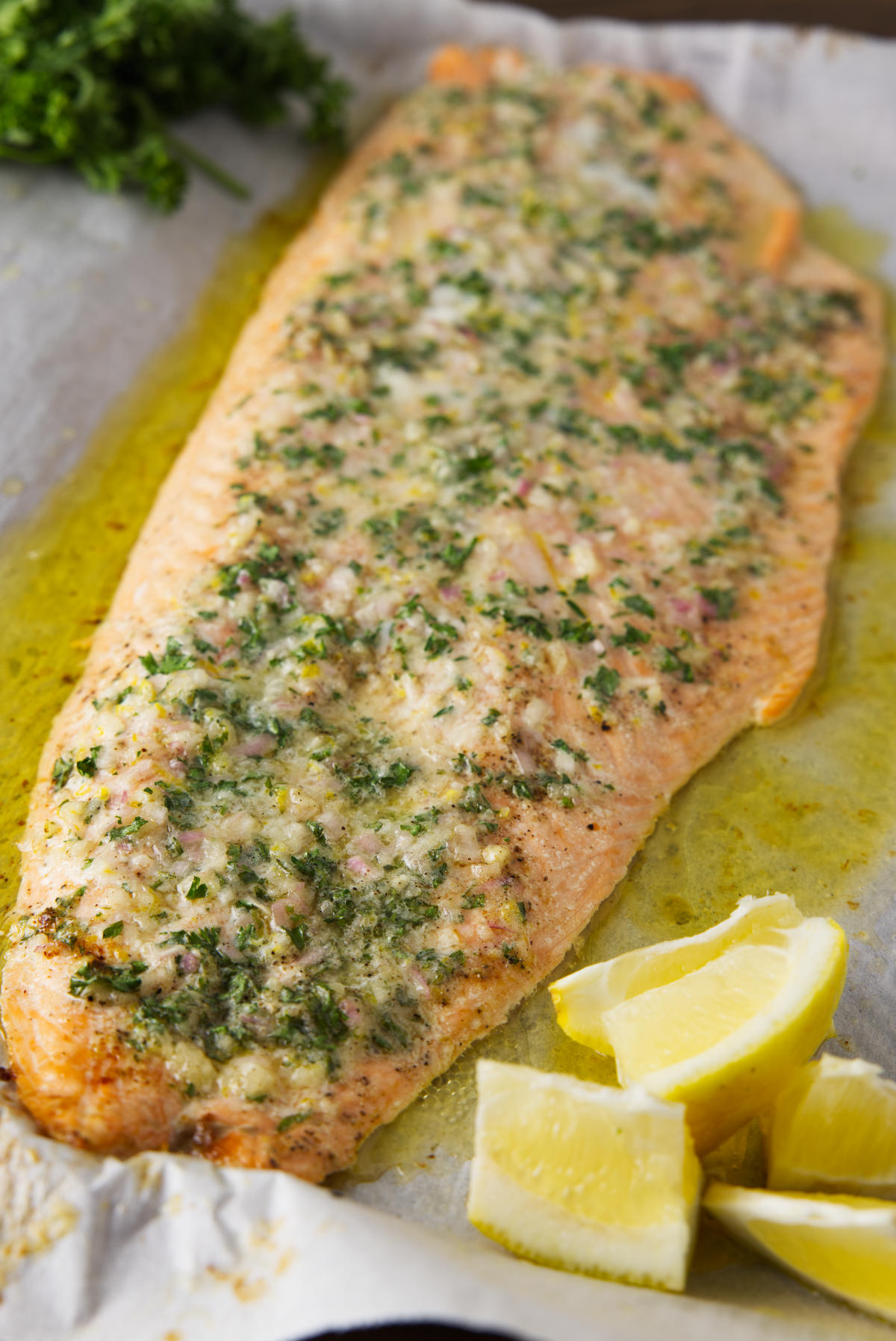 Salmon resting on sheet pan with lemon wedges and parsley.