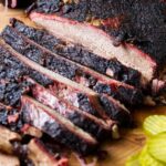 A smoked brisket on a cutting board next to pickles.