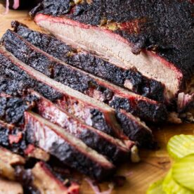 A smoked brisket on a cutting board next to pickles.