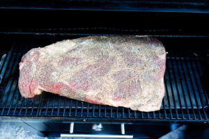 Placing a brisket on a hot pellet grill.