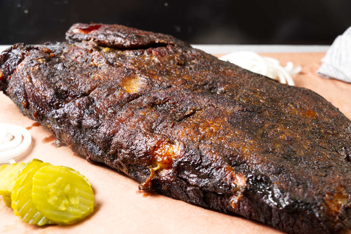 Smoked brisket on brown paper next to pickle slices.