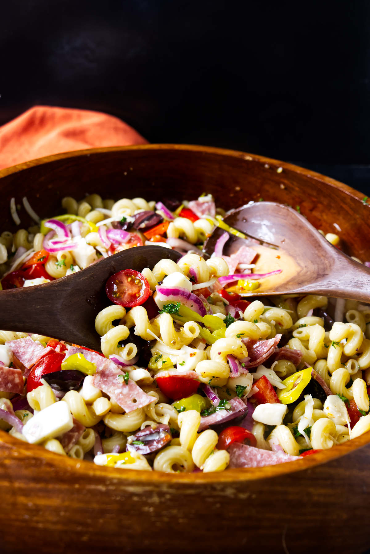 Tossing Italian pasta salad with large wooden utensils.
