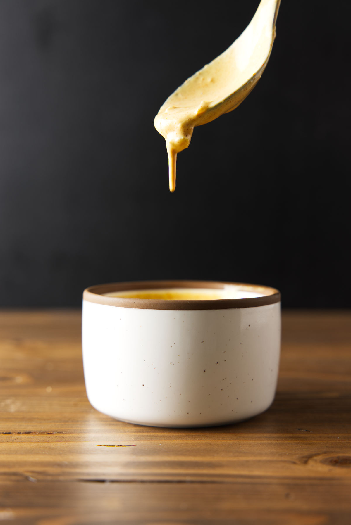 Smash burger sauce dripping from a spoon in to a bowl on a wood cutting board.