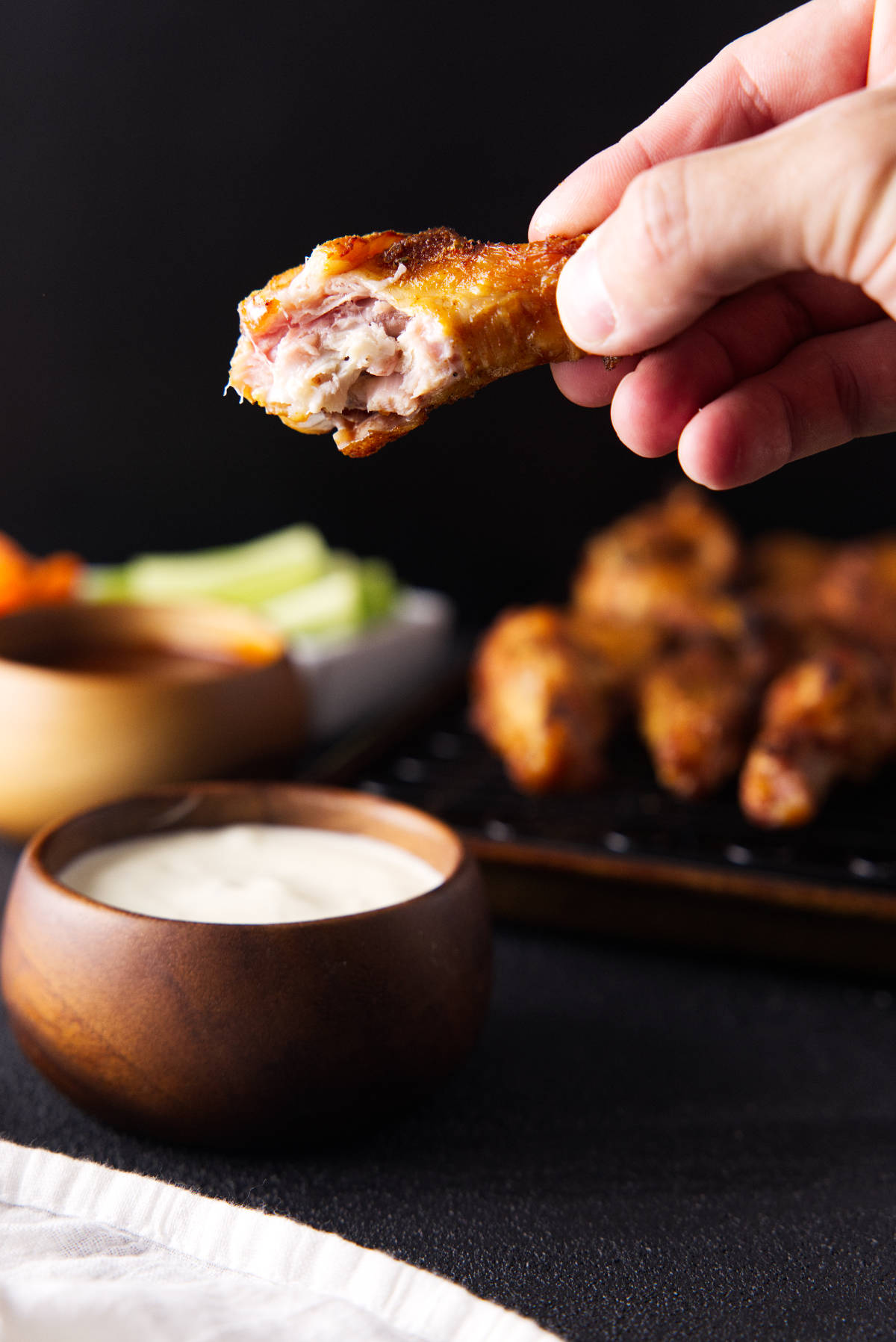 Hand holding a smoked chicken wing with a bite taken out of it.