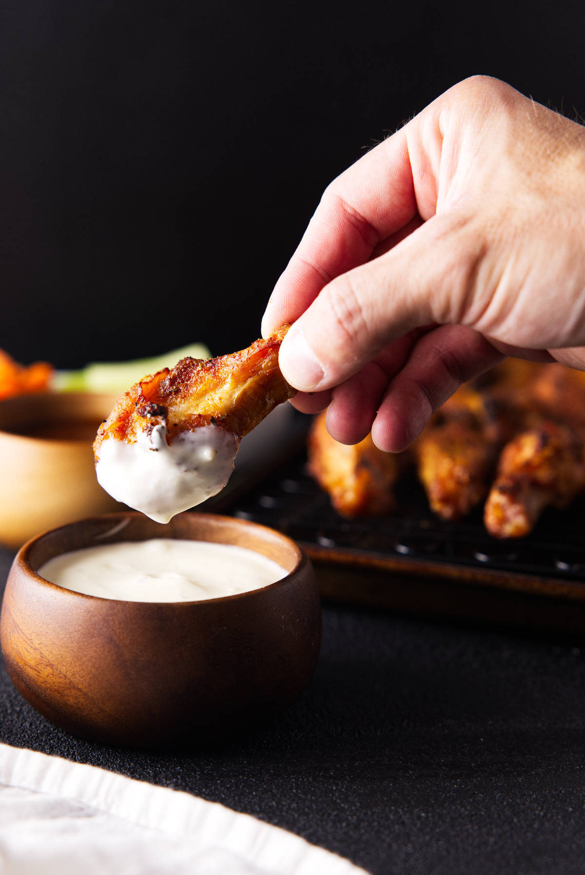 Dipping smoked chicken wing in blue cheese from a wooden bowl.