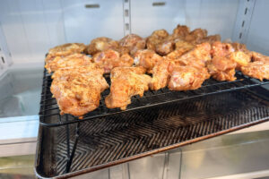 Seasoned chicken wings on a wire rack over a sheet pan resting in the fridge to dry out.
