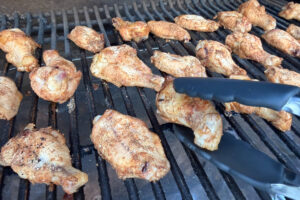 Turning chicken wings over with a pair of tongs on the Traeger grill grates.
