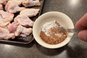 Mixing seasoning together next to chicken wings on a sheet pan.