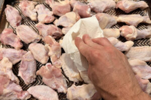 Patting chicken wings dry with a paper towel.
