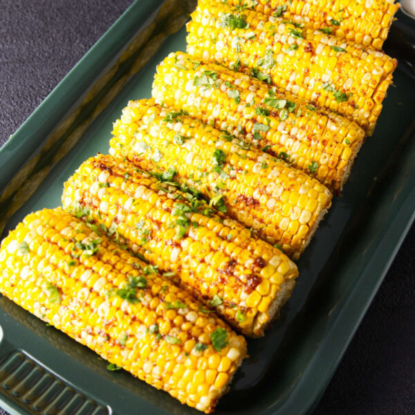 Smoked corn on the cob on a platter with barbecue seasoning and herbs.