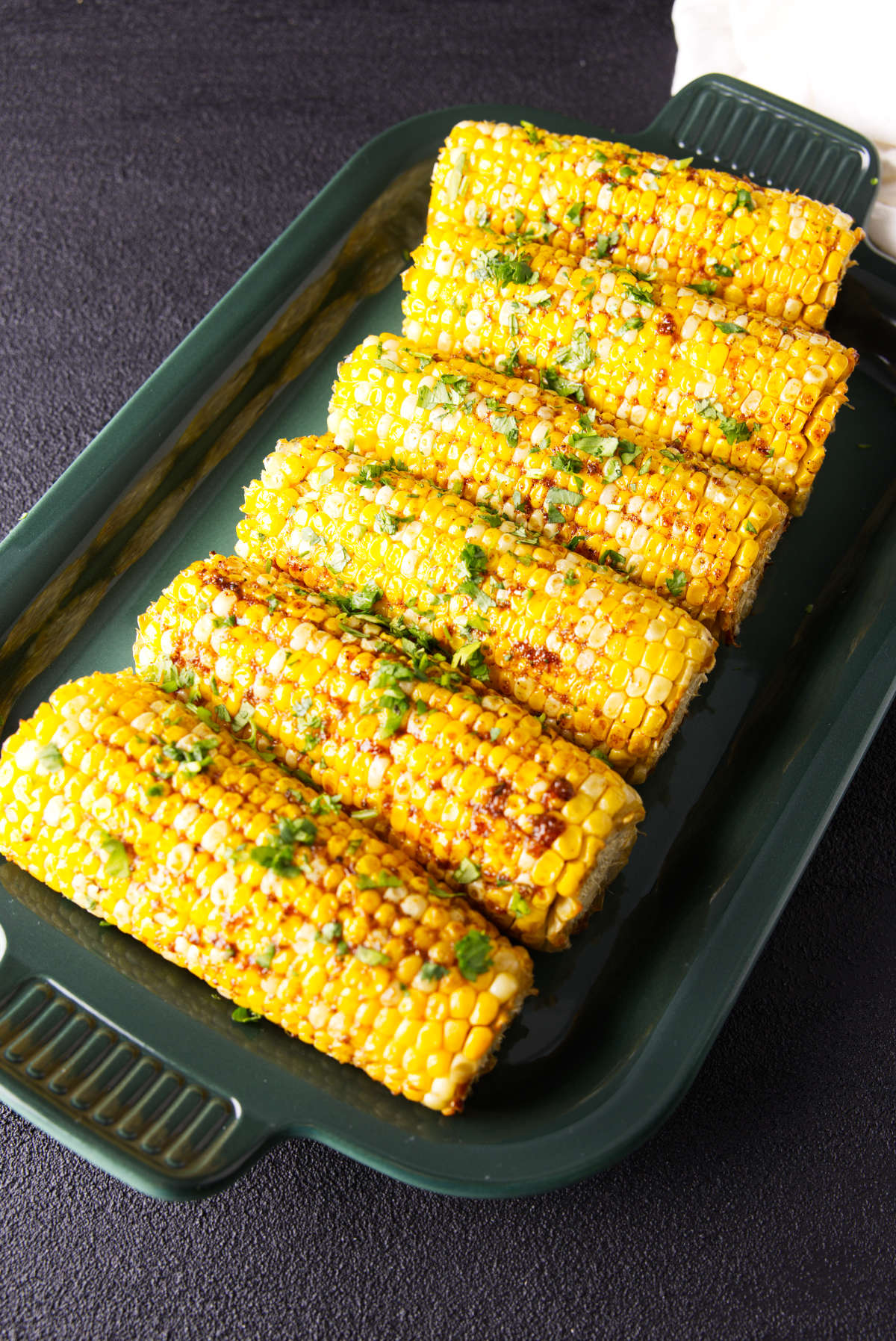 Smoked corn on the cob on a platter with barbecue seasoning and herbs.