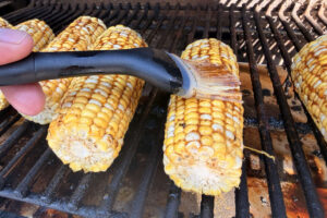 Basting smoked corn on the cob with barbecue butter on the pellet grill.