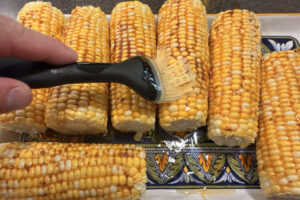Brushing corn on the cob with smoky barbecue butter before smoking.
