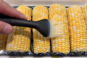 Brushing fresh corn on the cob with olive oil before smoking.