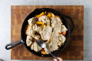 Spreading batter on top of peaches in a cast iron skillet.
