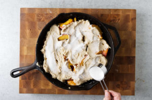 Topping the peach cobbler with sugar.