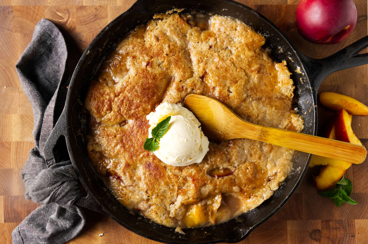 A wooden spoon and a scoop of ice cream on top of a hot peach cobbler.
