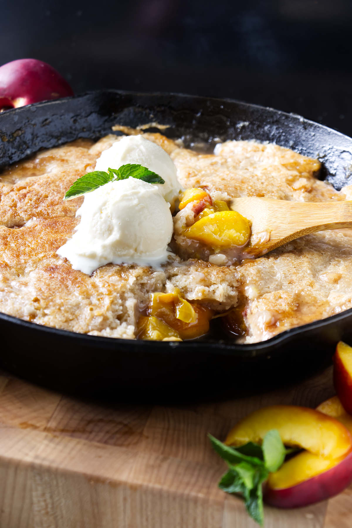 Scooping smoked peach cobbler from a cast iron skillet.