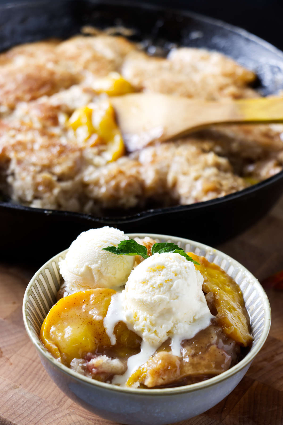 A bowl of pellet grill peach cobbler next to a cast iron skillet.