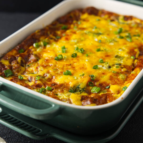 Crescent roll breakfast casserole in baking dish topped with melted cheese and chopped green onion.