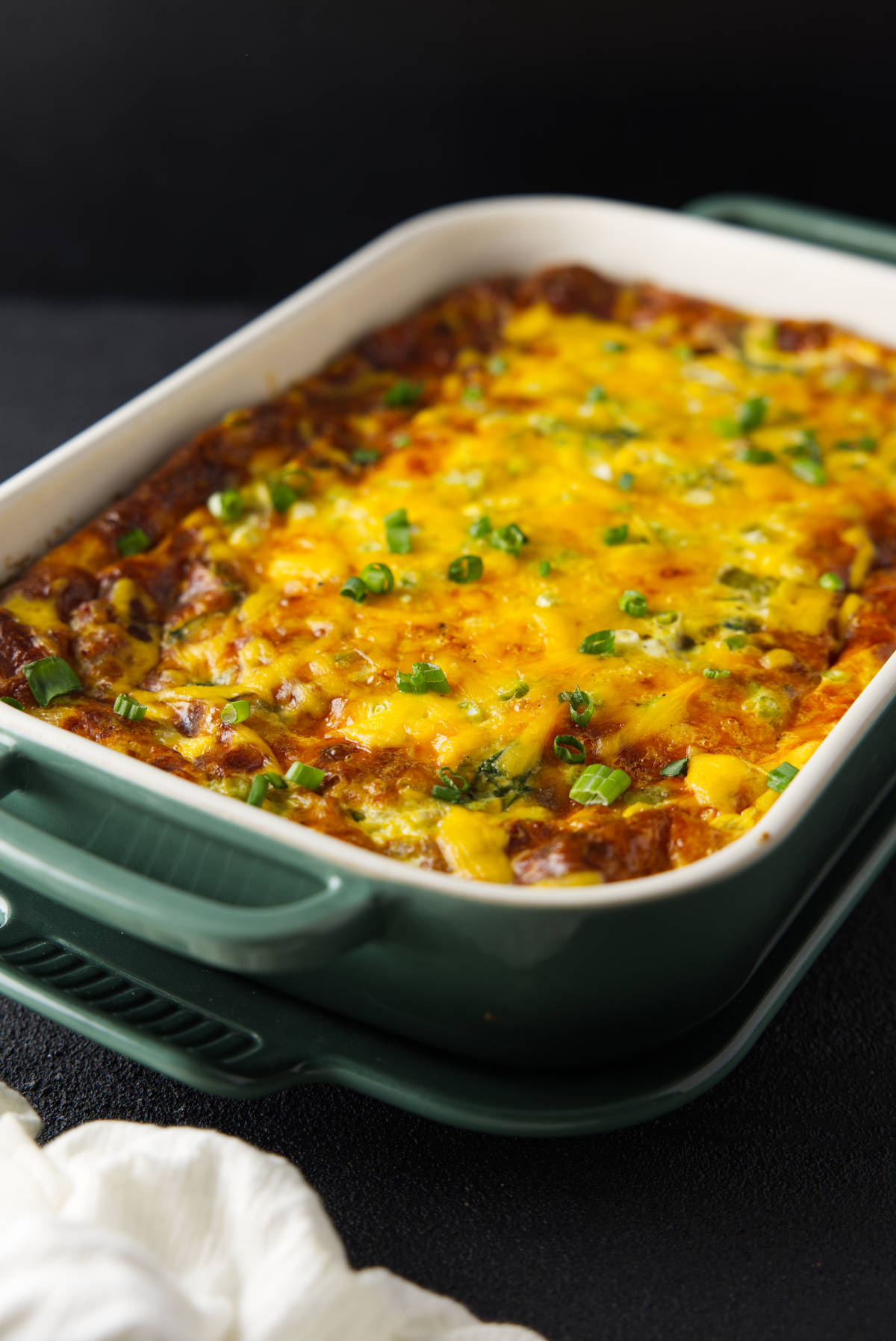 Golden crescent roll breakfast casserole with melted cheese and green onions in a green baking dish.
