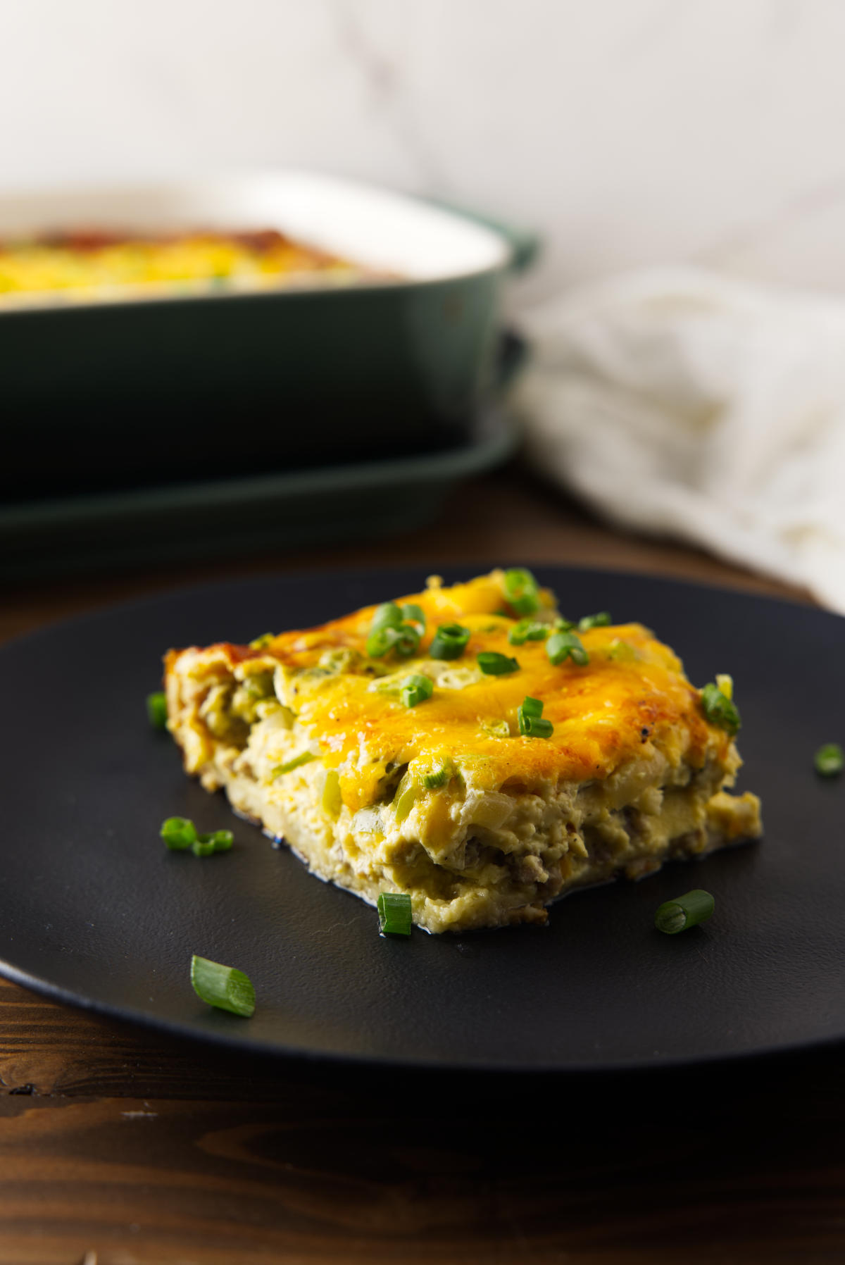 Slice of crescent roll breakfast casserole with sausage, vegetables, and melted cheese on a black plate.