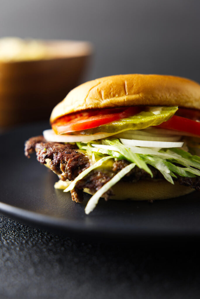Burger loaded with tomatoes, pickles, onions, and lettuce with melty cheese and crisp edges on the burger patty.