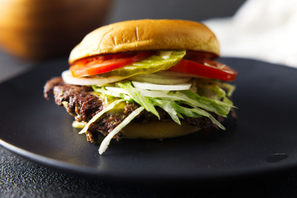Closeup shot of smash burger loaded with toppings and plated on a black plate.