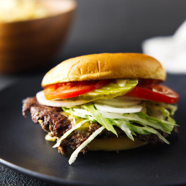 Smash burger loaded with tomatoes, onions, pickles, and lettuce, with melty cheese and on a black plate.