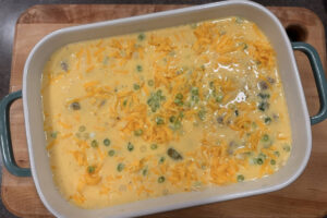 Assembled breakfast casserole in a baking dish, egg custard with green onions and cheddar cheese sprinkled on top.