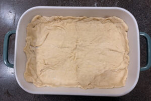 Sheet of Crescent roll dough spread out on the bottom of a baking dish.