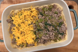 Browned and crumbled sausage layered on top of dough in a baking dish topped with sautéed veggies and cheddar cheese.
