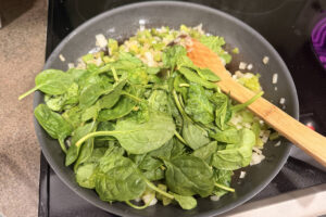 Large sauté pan with onions, bell pepper, and spinach cooking down.