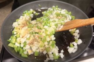 Diced onion and bell pepper in a sauté pan with seasoning sprinkled on top.