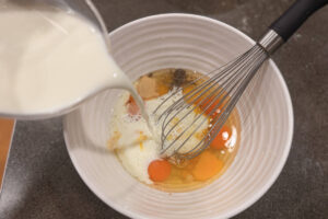 Whisking eggs together in a large bowl with milk and seasoning.